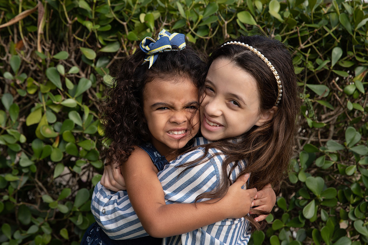 Ensaio de bebê: irmãs da Ester se abraçando no jardim no Rio de Janeiro.