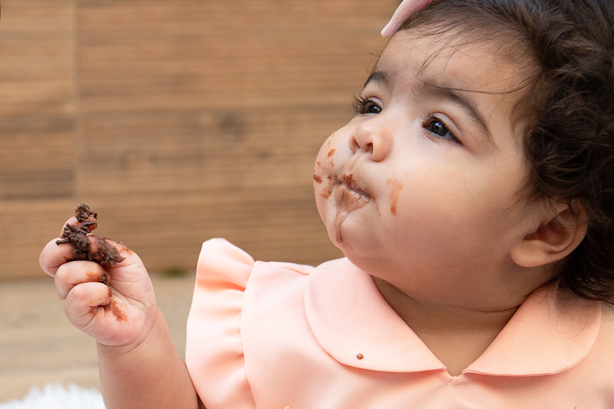 Ensaio de bebê: Ester com a mão e boca sujas de bolo no Rio de Janeiro.