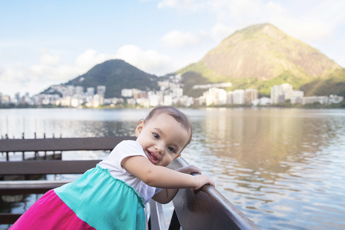 Ensaio de Família no Clube Piraquê: Laura no banco com a Lagoa ao fundo, no Rio de Janeiro.