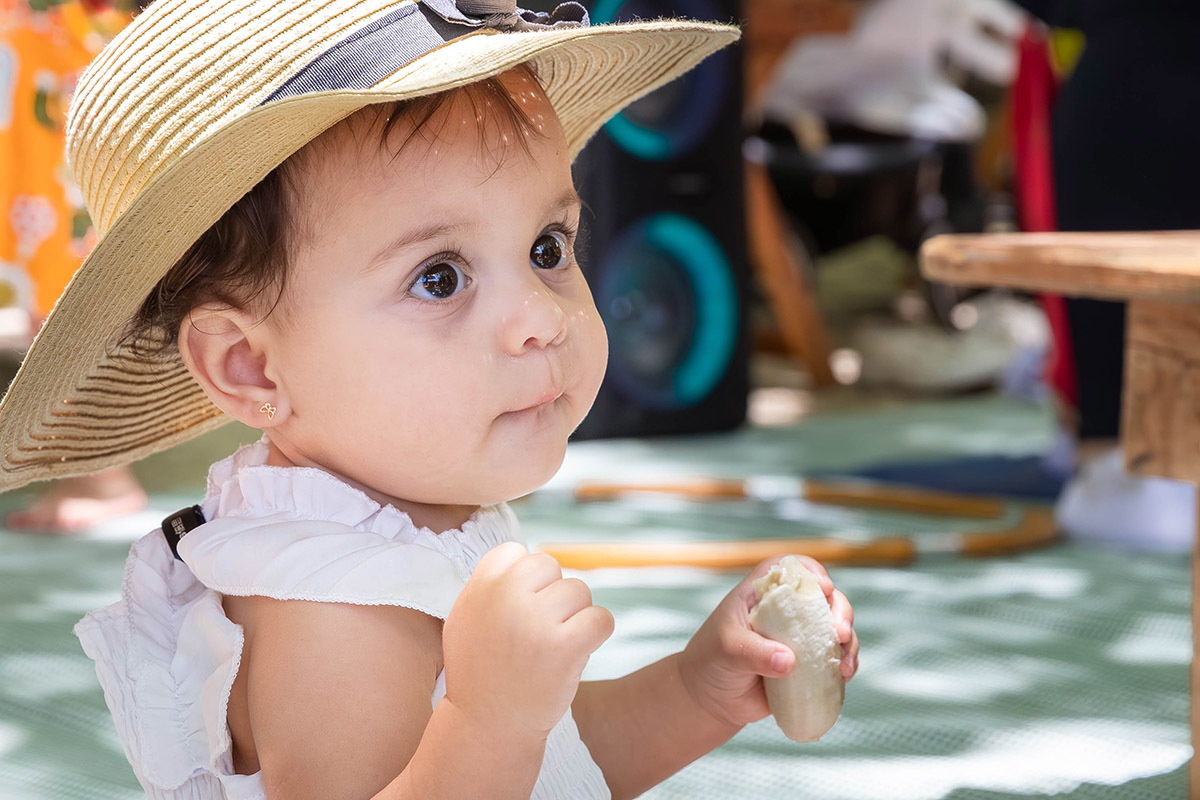 Alice de chapéu de palha comendo banana em sua festa Piquenique na lagoa no Rio de Janeiro