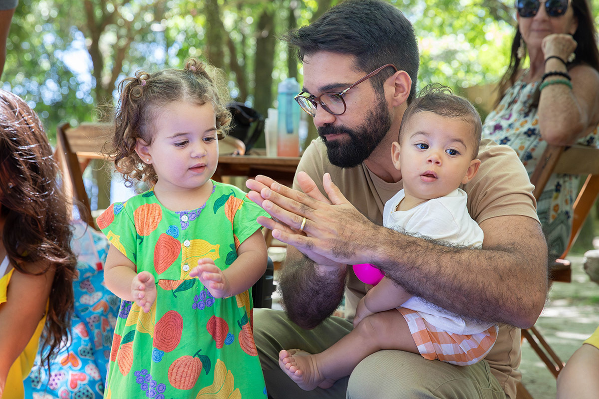 Pai brincando com de palmas com as filhas durante a festa da Alice na Lagoa no Rio de Janeiro