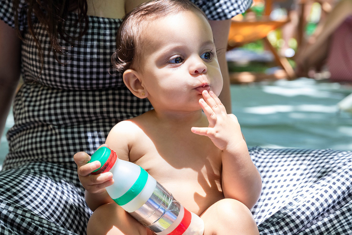 Alice no colo da mãe e dedo na boca em sua festa Piquenique na Lagoa