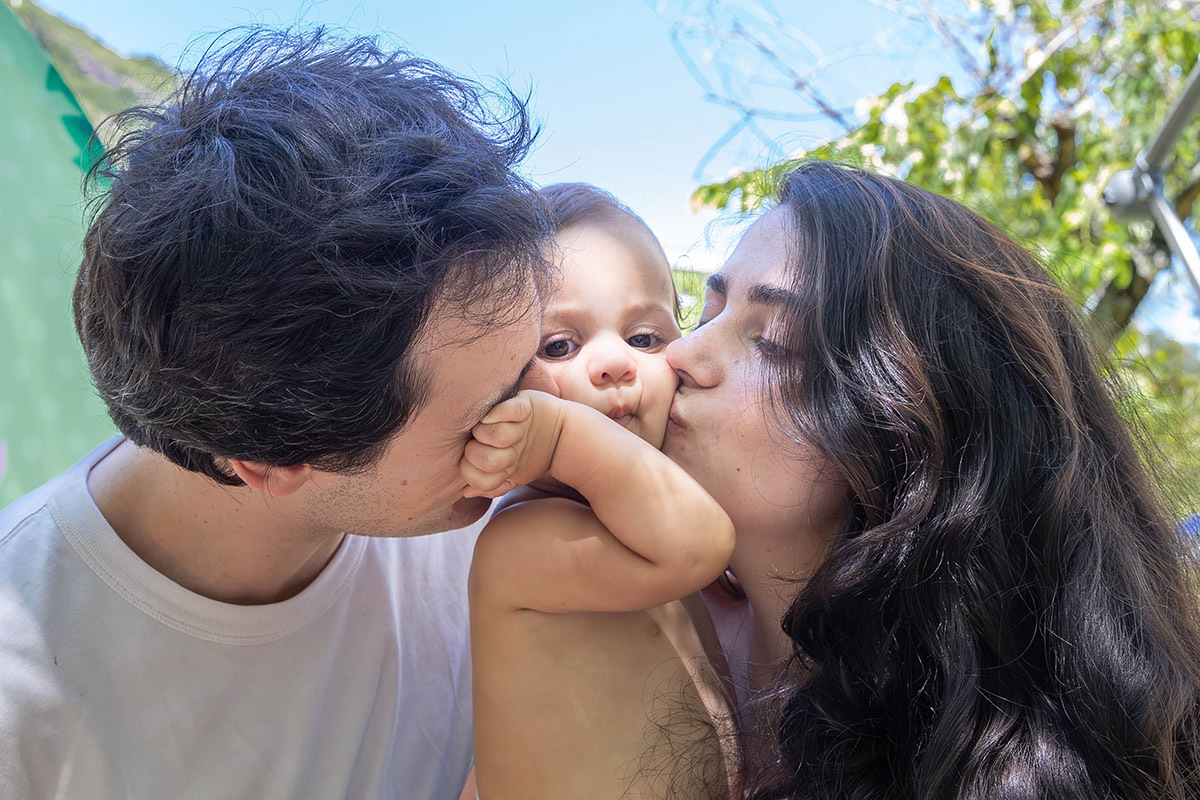Alice recebendo beijo da mãe e do pai ao mesmo tempo em seu aniversário de um ano na Lagoa no Rio de janeiro