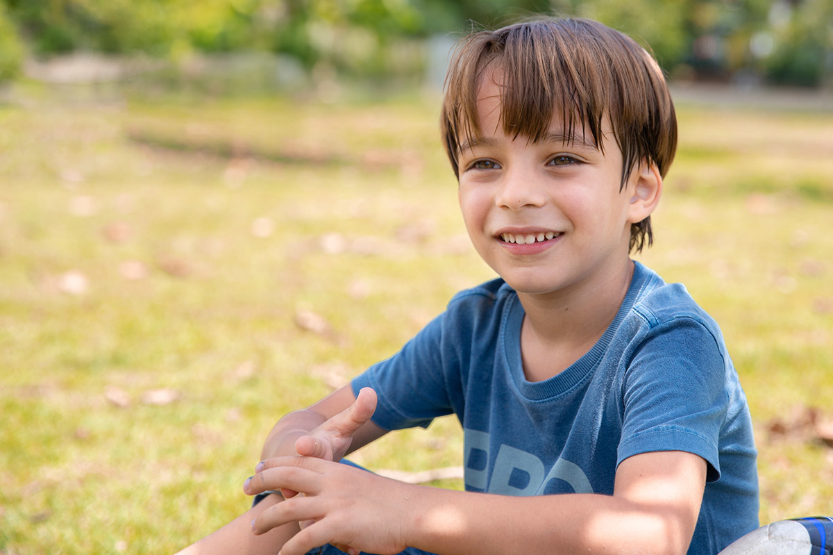 Menino sentado na grama sorrindo no ensaio de família na Lagoa

