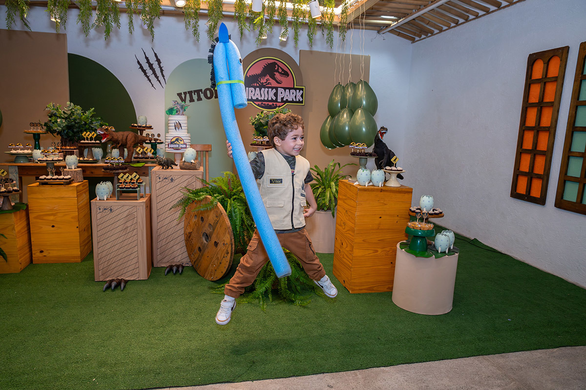 aniversariante pulando em rente a mesa do bolo da festa infantil tema jurassic park