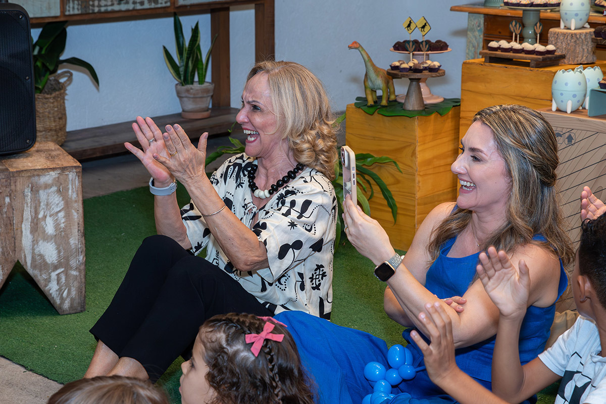 mae e avó aplaudindo a apresentação mágico Rogê na festa infantil