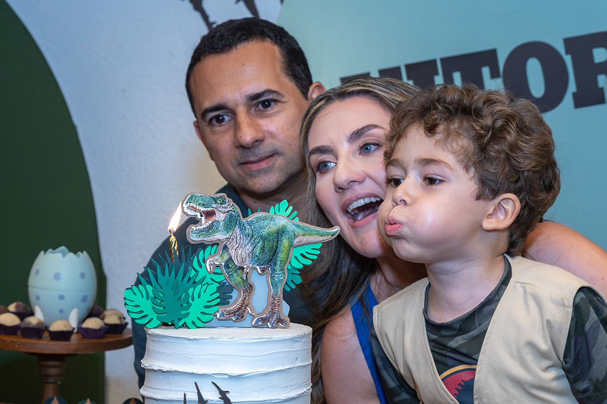 Aniversariante soprando a vela do bolo ao lado do pai e da mãe durante a festa infantil no espaço aldeia