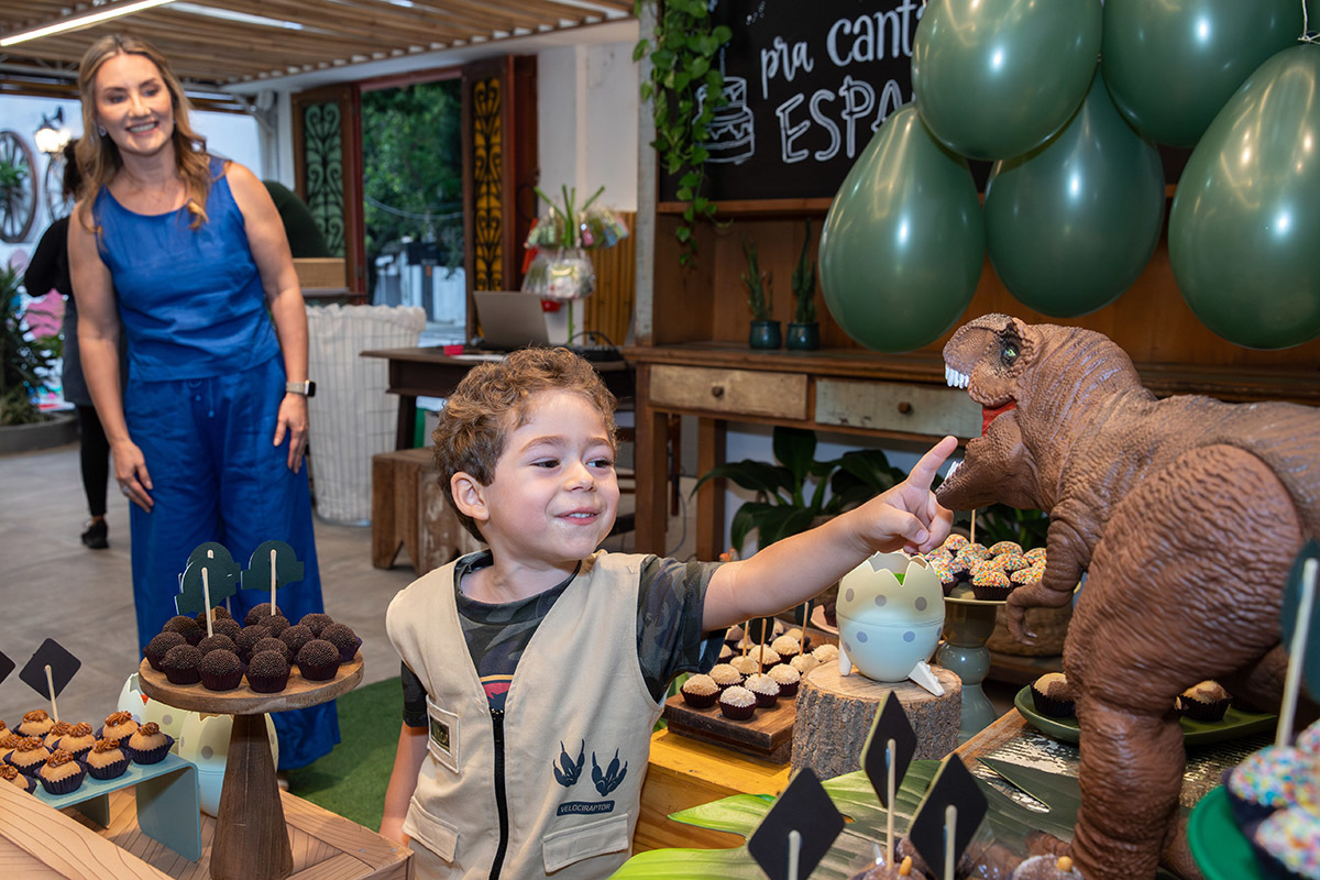 Aniversariante se divertindo com o bolo temático de dinossauros no Espaço Aldeia

