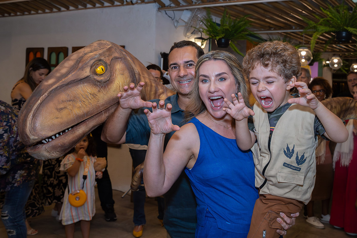 mae, pai e aniversariante brincando com o personagem dinossauro em festa  infantil no Espaço Aldeia