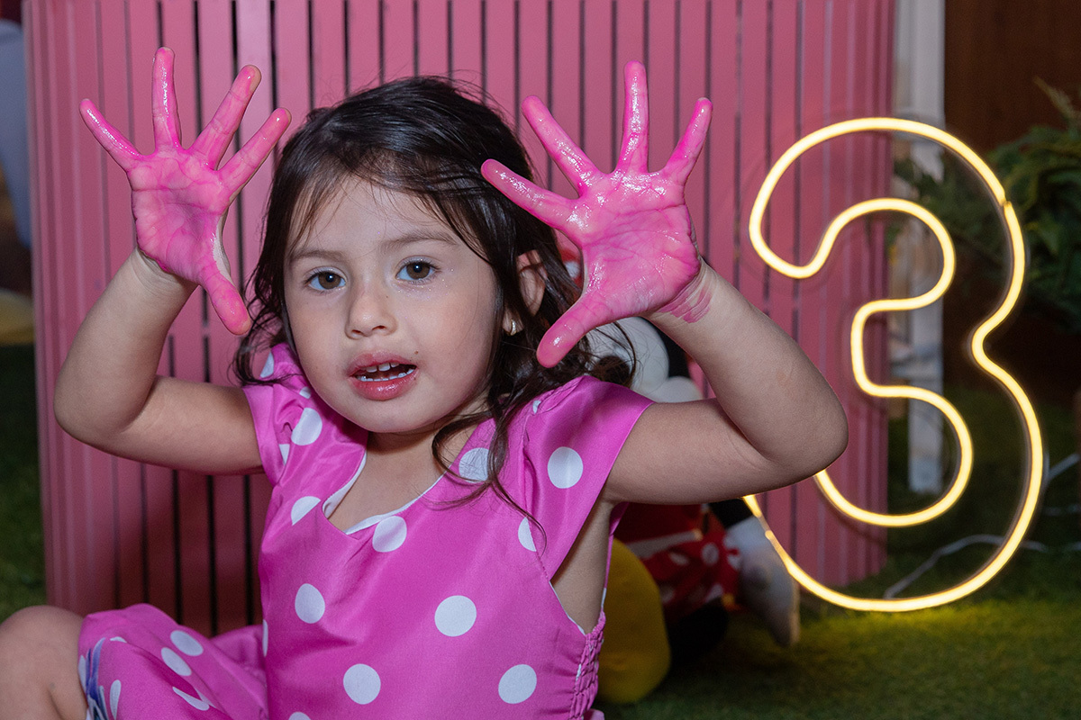 Aniversariante sorridente com fantasia da Minnie com as mãos sujas de tinta durante festa na Espoleta