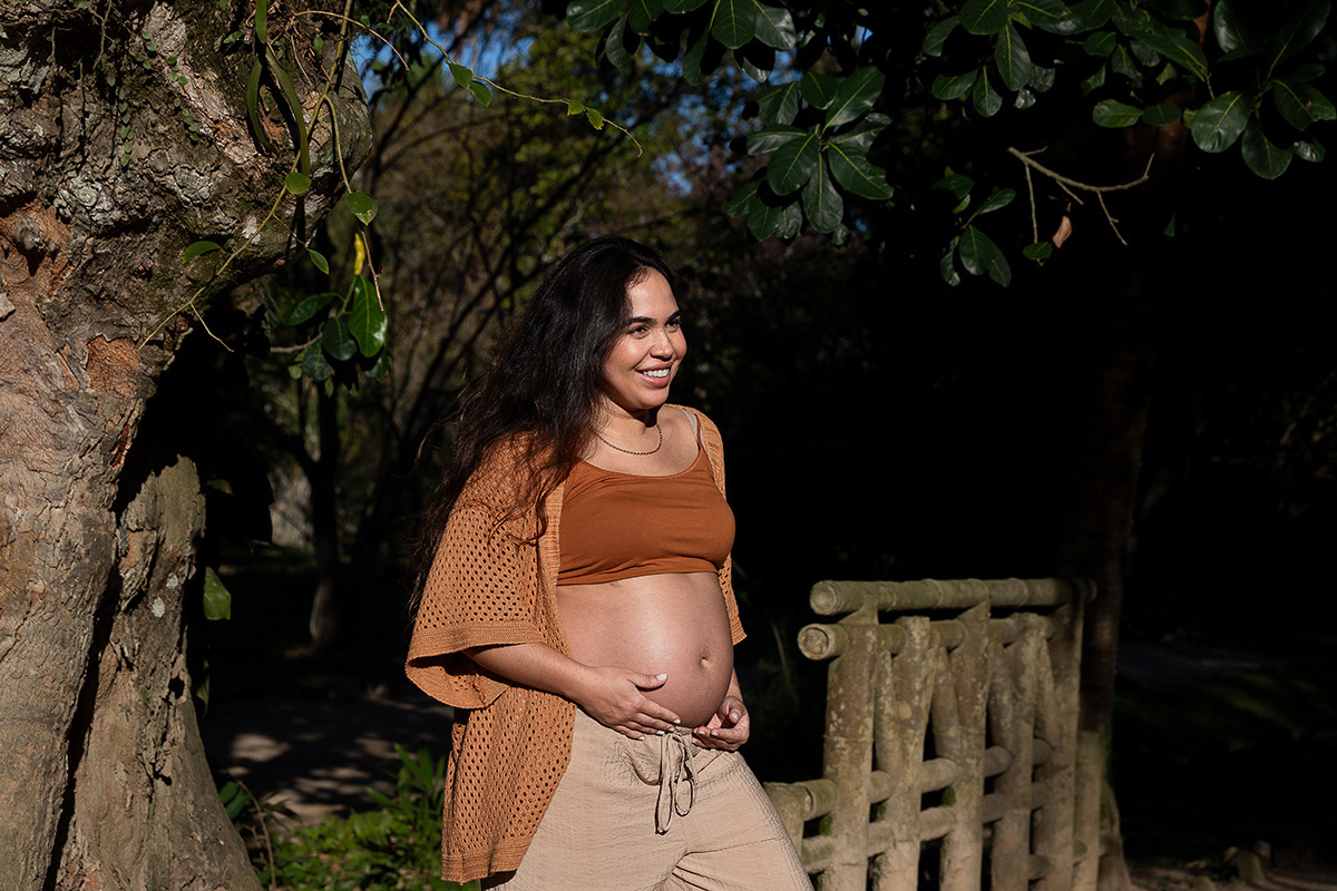 Luz suave da manhã iluminando gestante sorrindo em ensaio no jardim botanico