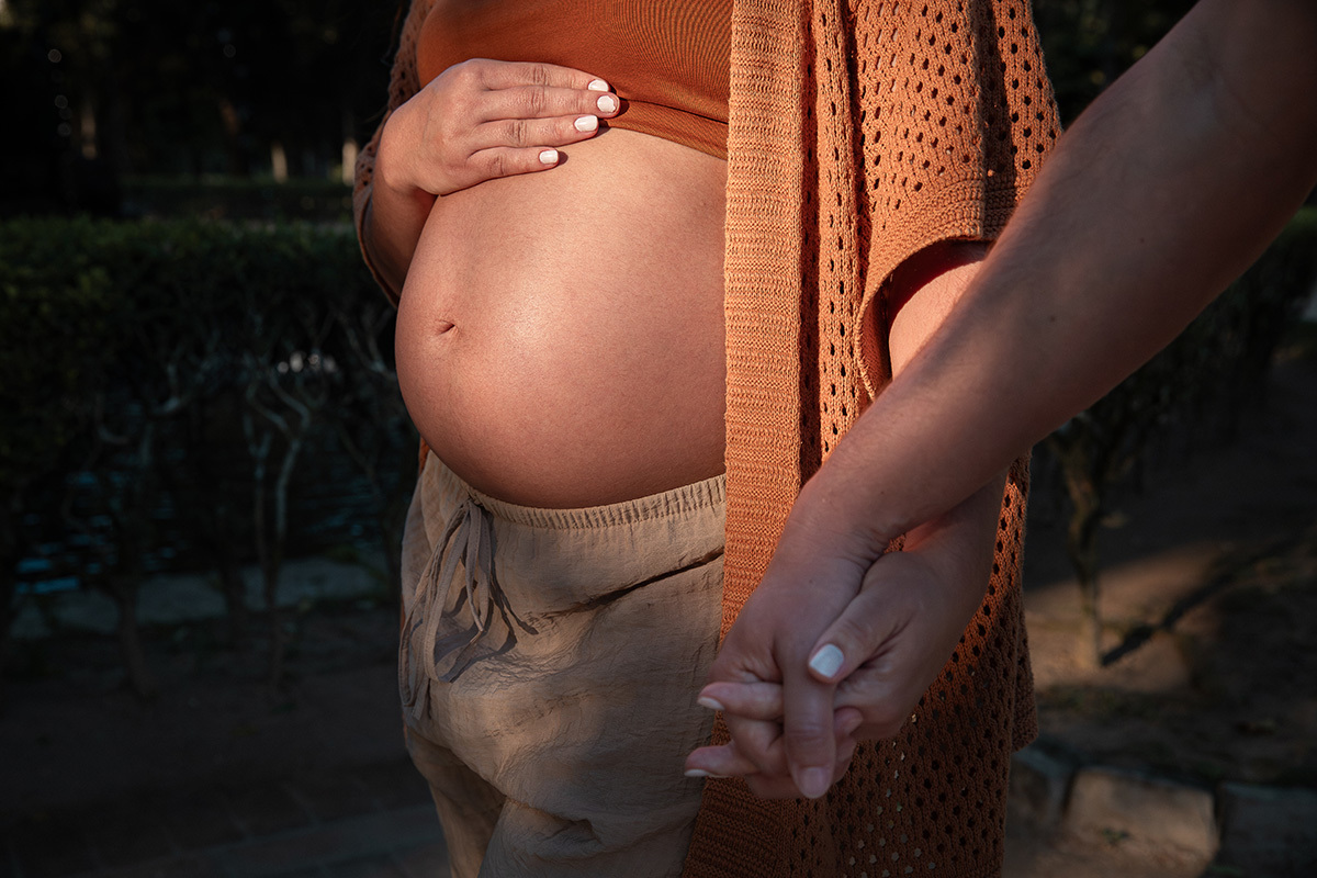 detalhe da barriga da gestante de mãos dadas com o marido com luz dourada