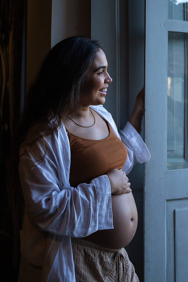 gestante sorrindo com a luz da janela em seu rosto