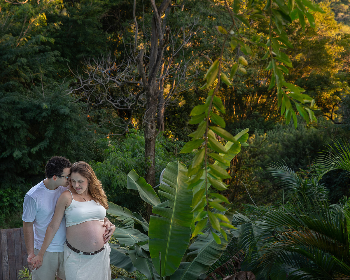 Casal caminhando entre o jardim durante ensaio gestante em uma casa integrada à natureza.