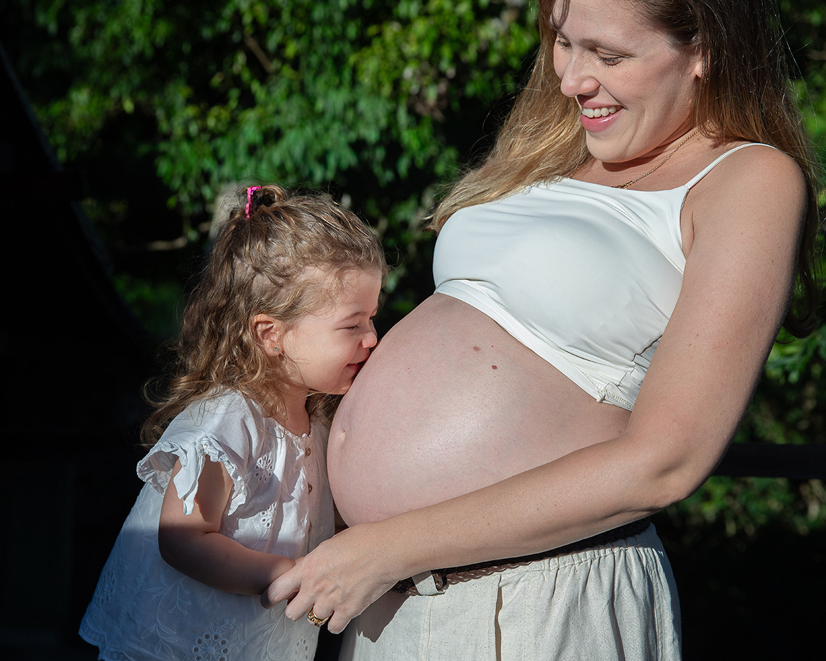 A filha beija a barriga da mãe durante um emocionante ensaio gestante em família.