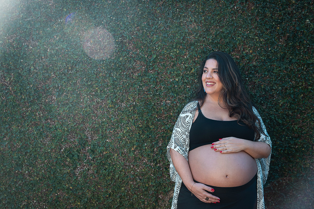 Retrato da gestante com luz natural  em frente ao muro com plantas no Rio de Janeiro