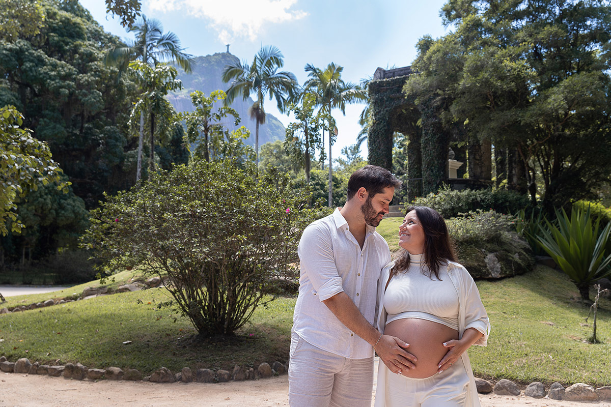 Casal abraçados durante o ensaio de gestante no jardim botânico com o Cristo Redentor ao fundo