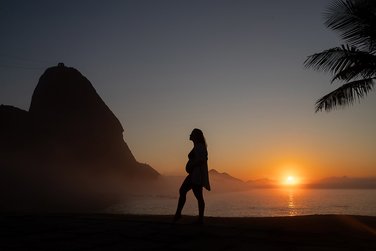 silhueta de gestante com céu laranja ao amanhecer na Praia vermelha