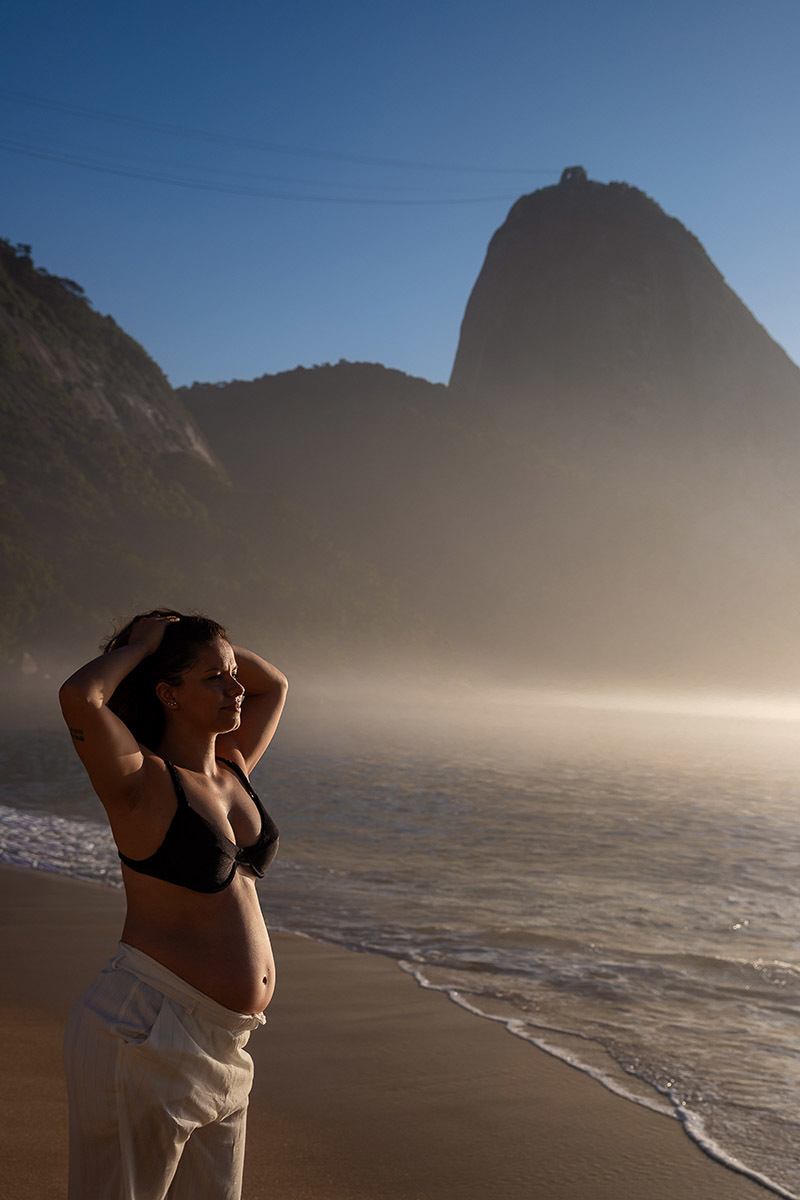 grávida na Praia Vermelha durante o amanhecer, com o mar e o Morro da Urca ao fundo.