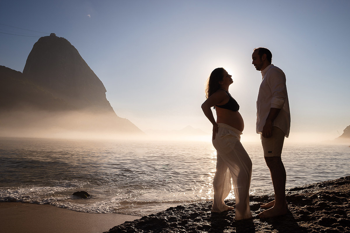 Silhueta de casal durante ensaio gestante na Praia Vermelha com o mar e morro da Urca ao fundo
