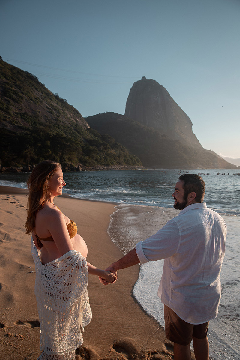Casal sorrindo se olhando com o mar ao fundo durante ensaio na Praia Vermelha