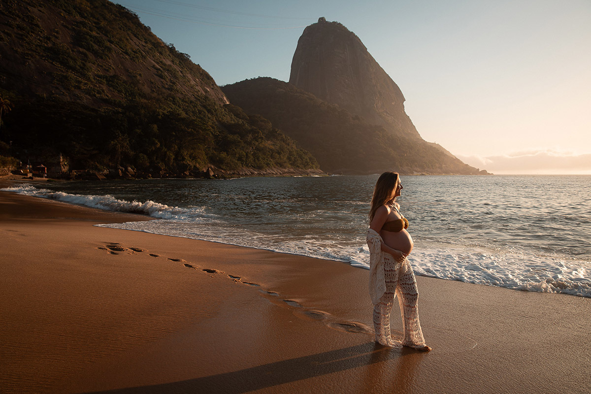 Gestante com pegadas na areia e mar ao fundo durante ensaio na Praia Vermelha