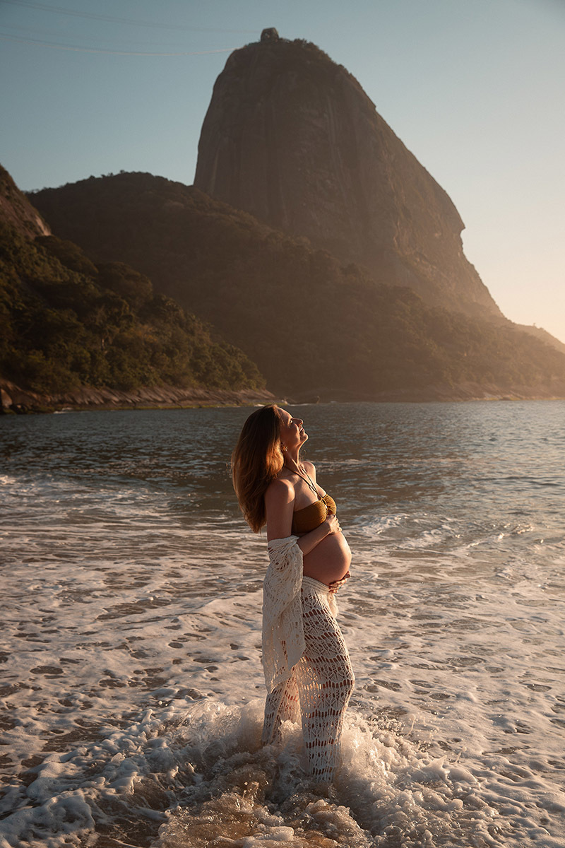 Gestante com as mãos na barriga plena durante ensaio na Praia Vermelha