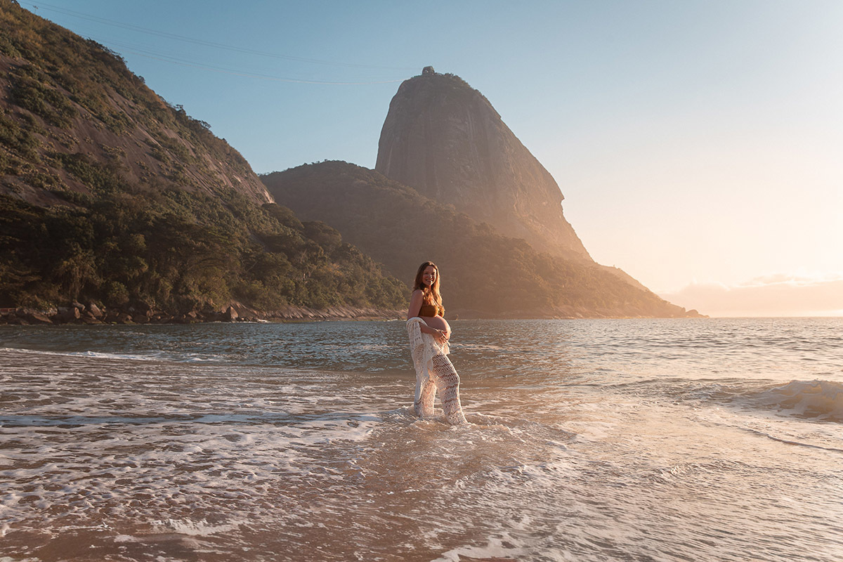 Gestante com os pes na agua do mar da Praia Vermelha e morro da urca ao fundo
