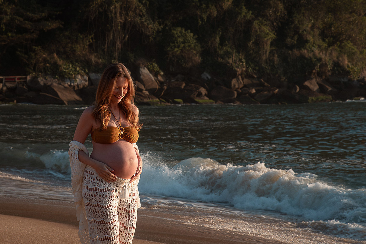 Gestante acariciando a barriga enquanto anda na areia na Priaa Vermelha
