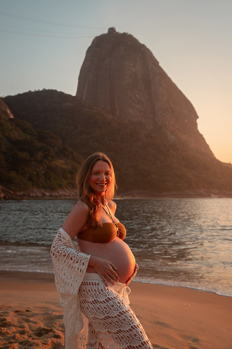 gestante sorrindo com luz do nascer do sol durante ensaio na Praia Vermelha