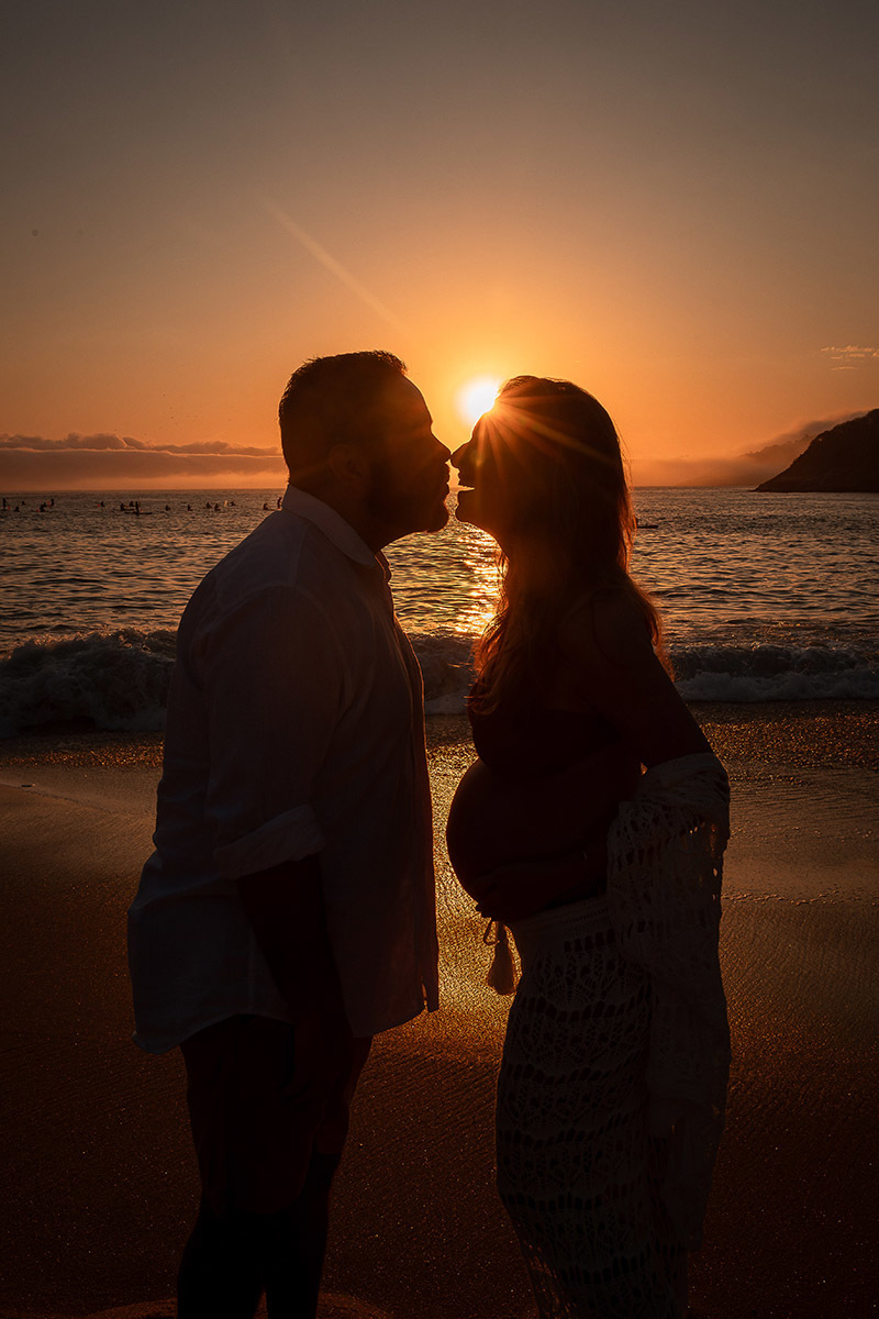 Foto artística de silhueta de casal gestante com fundo laranja do amanhecer.