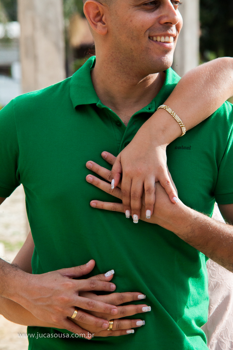 Noiva abraçando seu noivo por trás de mãos dadas e destacando suas alianças de noivado