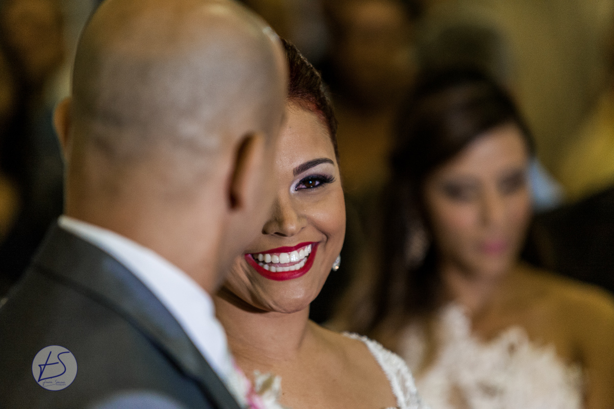 Ao encontrar o noivo no final do tapete vermelho a noiva solta um largo sorriso para o seu amado que acaba de recebe-la do pai