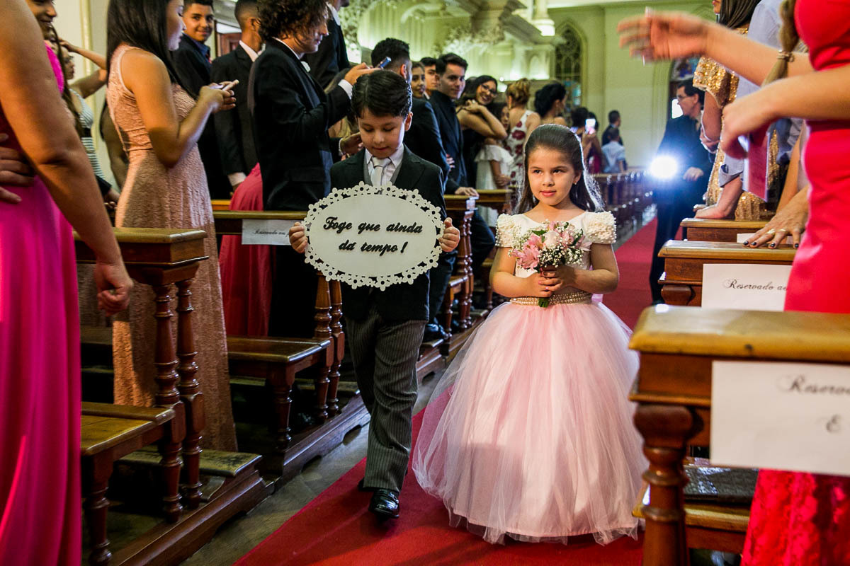 dama e pagem entrando pela igreja, a dama de honra segura um bouquet de flores e o pajem segura uma placa com os dizeres foge que ainda dá tempo