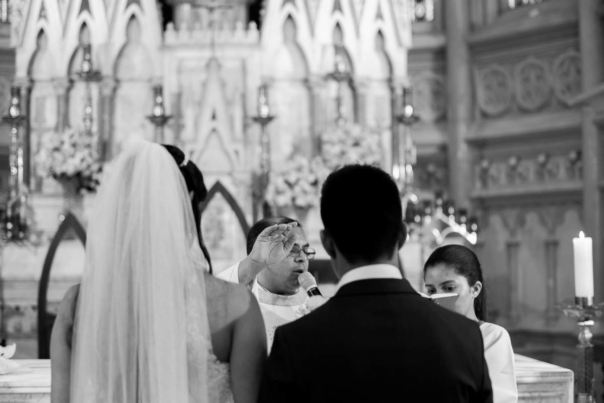 foto em preto e branco tirada por juca sousa, do padre com a mão erguida a abençoar o casal recém casado