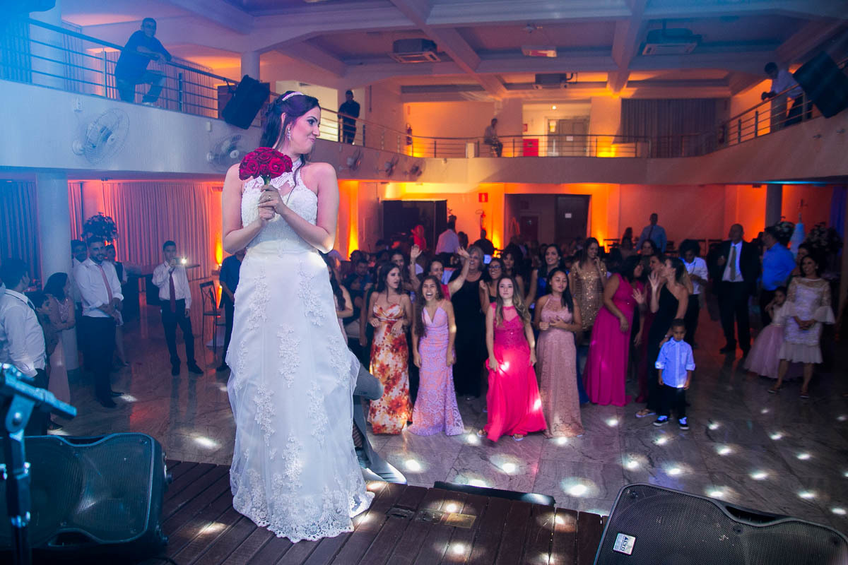 noiva em cima do palco segurando o bouquet pronta para jogar para as amigas ao fundo