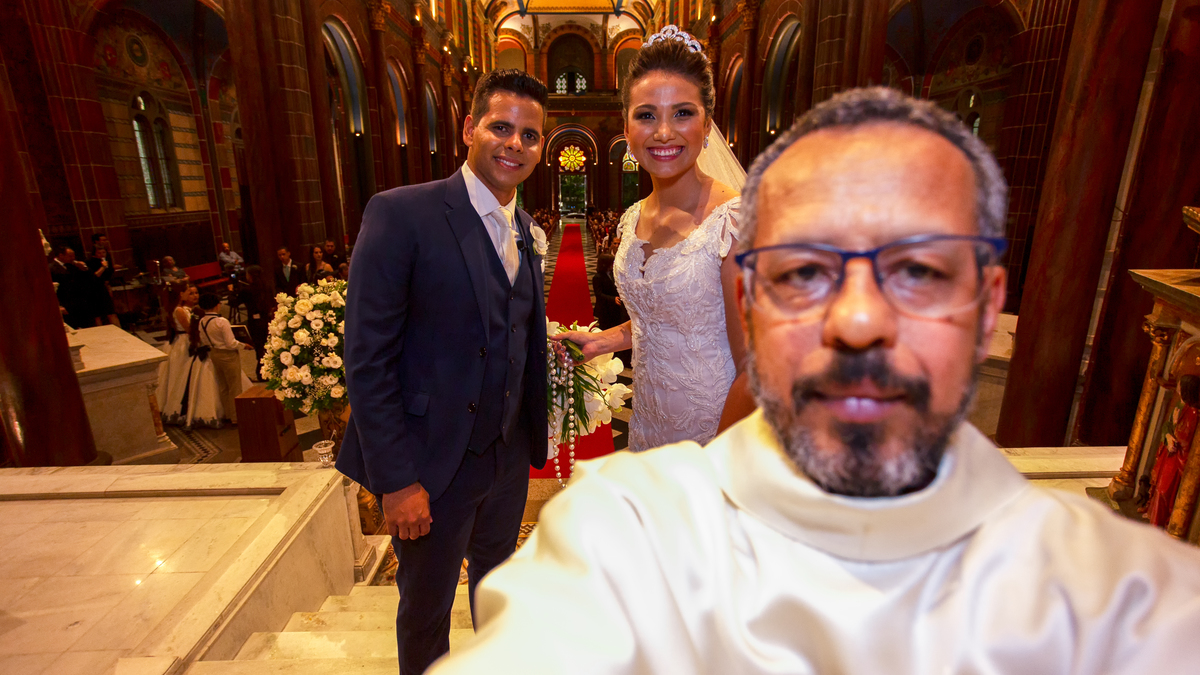 o celebrante da igreja são josé de belo horizonte pega a máquina do fotógrafo para fazer uma selfie com os noivos