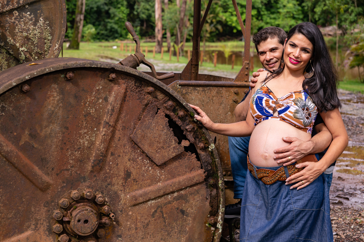 casal gestante abraçados ele com a mão na barriga dela e ela com a mão na roda do trator fazenda arraial velho