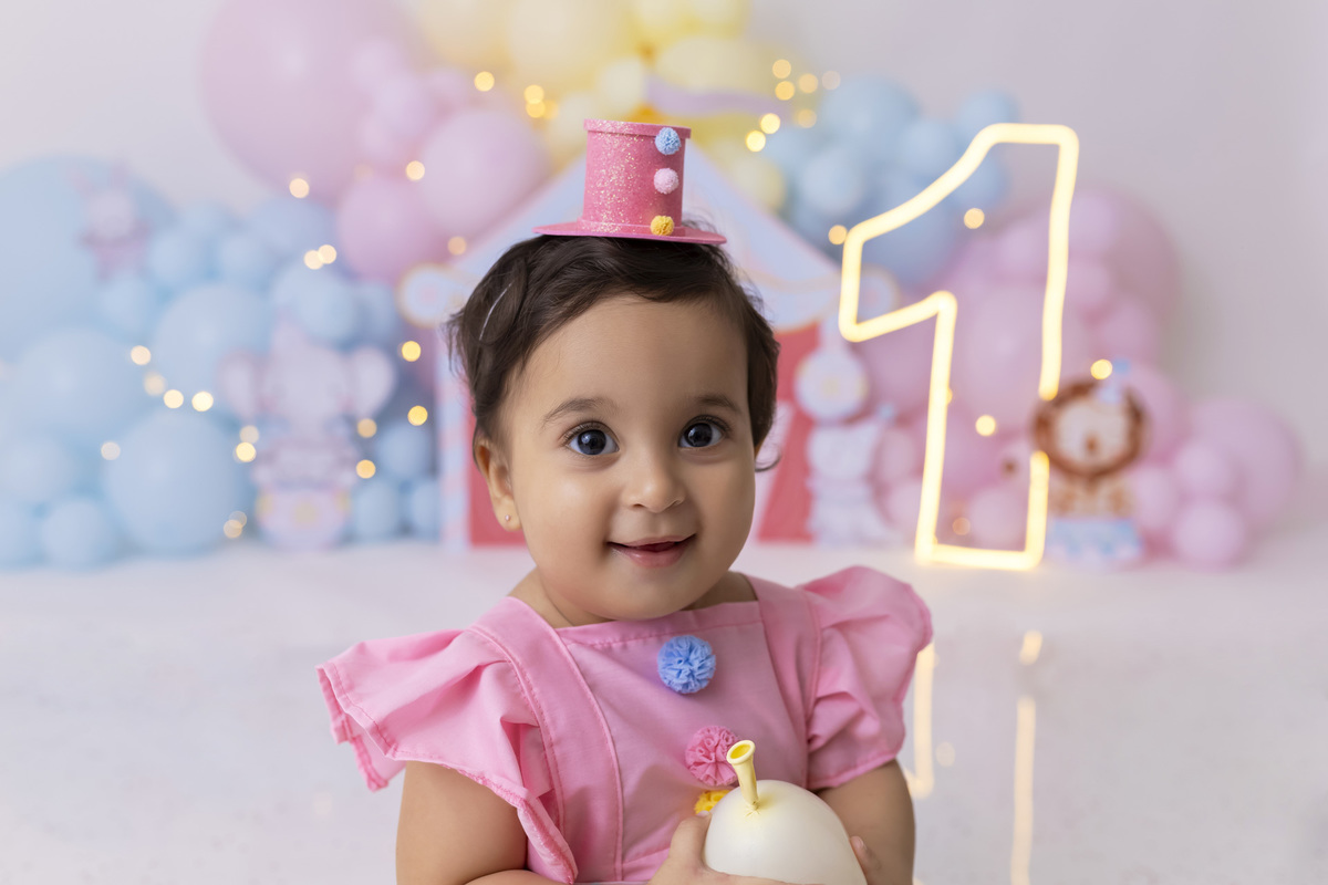 Bebê em ensaio Smash the Cake tema circo em estúdio fotográfico em Caraguatatuba, cenário colorido personalizado, bolo decorado, criança sorrindo e se divertindo durante sessão infantil