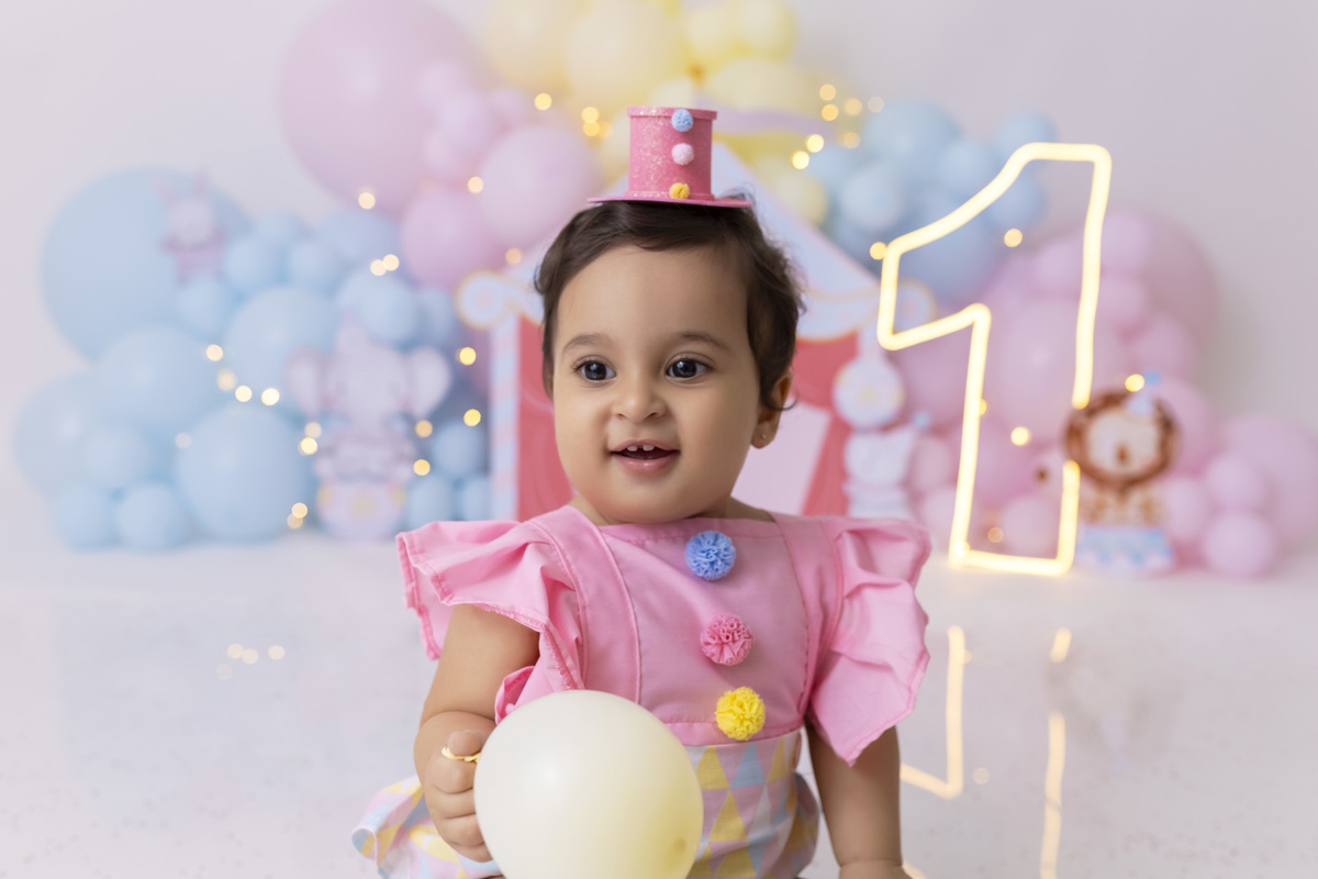 Bebê em ensaio Smash the Cake tema circo em estúdio fotográfico em Caraguatatuba, cenário colorido personalizado, bolo decorado, criança sorrindo e se divertindo durante sessão infantil