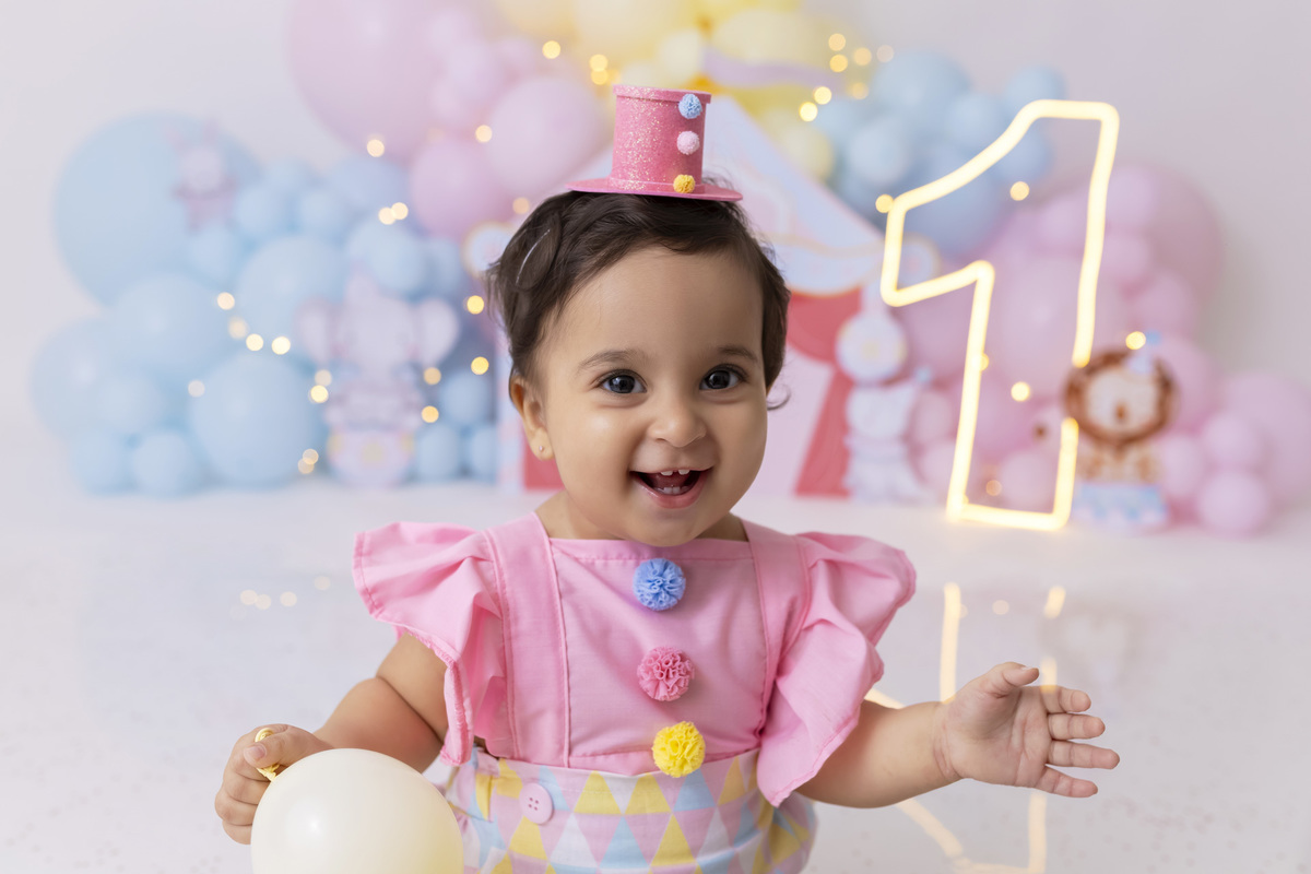 Bebê em ensaio Smash the Cake tema circo em estúdio fotográfico em Caraguatatuba, cenário colorido personalizado, bolo decorado, criança sorrindo e se divertindo durante sessão infantil