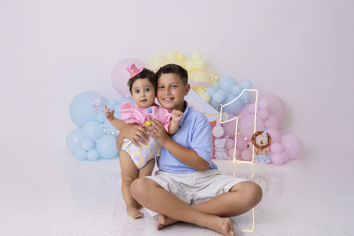 Bebê em ensaio Smash the Cake tema circo em estúdio fotográfico em Caraguatatuba, cenário colorido personalizado, bolo decorado, criança sorrindo e se divertindo durante sessão infantil