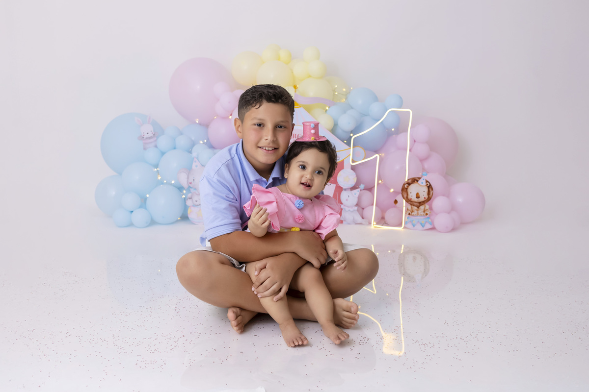 Bebê em ensaio Smash the Cake tema circo em estúdio fotográfico em Caraguatatuba, cenário colorido personalizado, bolo decorado, criança sorrindo e se divertindo durante sessão infantil