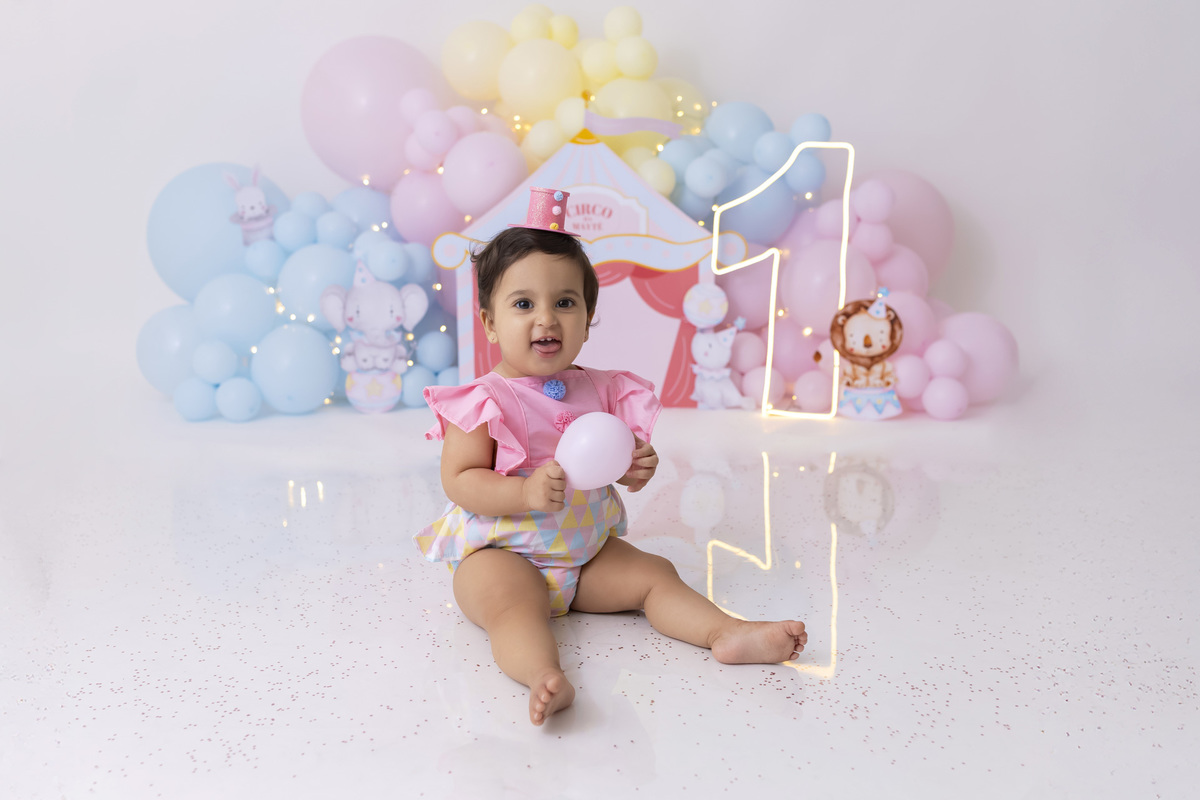 Bebê em ensaio Smash the Cake tema circo em estúdio fotográfico em Caraguatatuba, cenário colorido personalizado, bolo decorado, criança sorrindo e se divertindo durante sessão infantil