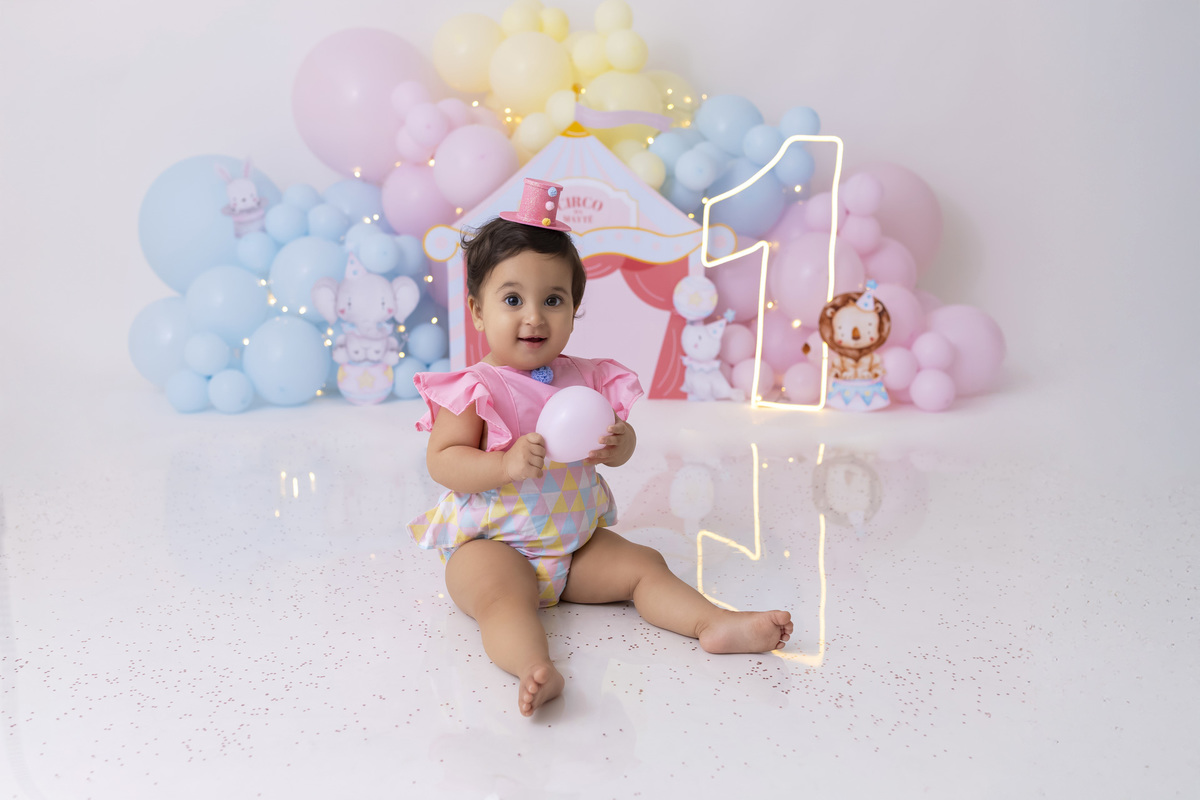 Bebê em ensaio Smash the Cake tema circo em estúdio fotográfico em Caraguatatuba, cenário colorido personalizado, bolo decorado, criança sorrindo e se divertindo durante sessão infantil