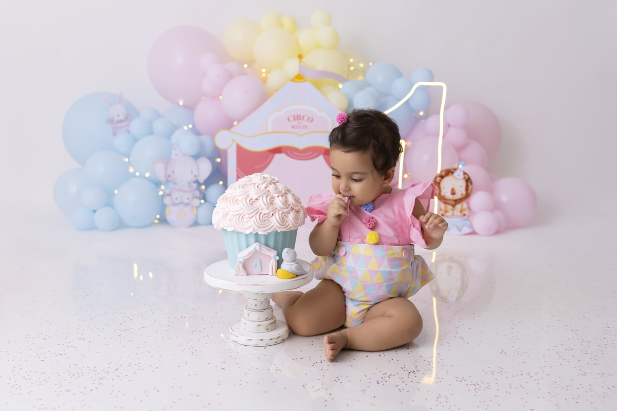 Bebê em ensaio Smash the Cake tema circo em estúdio fotográfico em Caraguatatuba, cenário colorido personalizado, bolo decorado, criança sorrindo e se divertindo durante sessão infantil