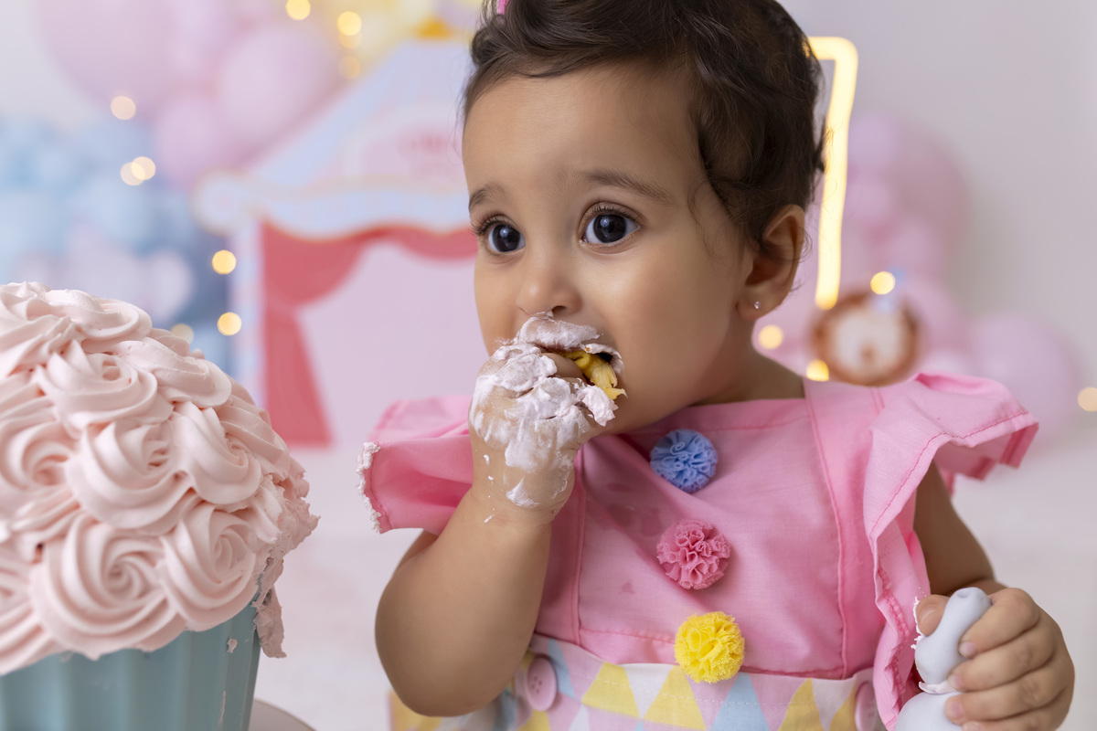 Bebê em ensaio Smash the Cake tema circo em estúdio fotográfico em Caraguatatuba, cenário colorido personalizado, bolo decorado, criança sorrindo e se divertindo durante sessão infantil