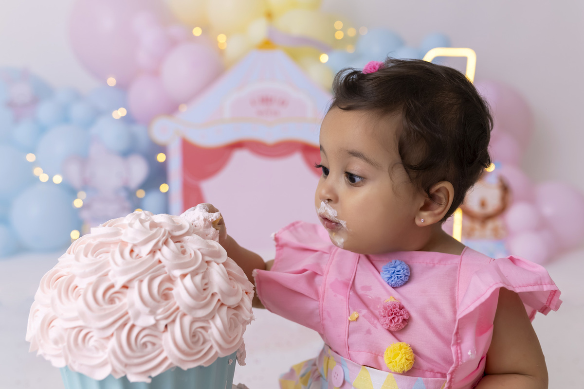 Bebê em ensaio Smash the Cake tema circo em estúdio fotográfico em Caraguatatuba, cenário colorido personalizado, bolo decorado, criança sorrindo e se divertindo durante sessão infantil