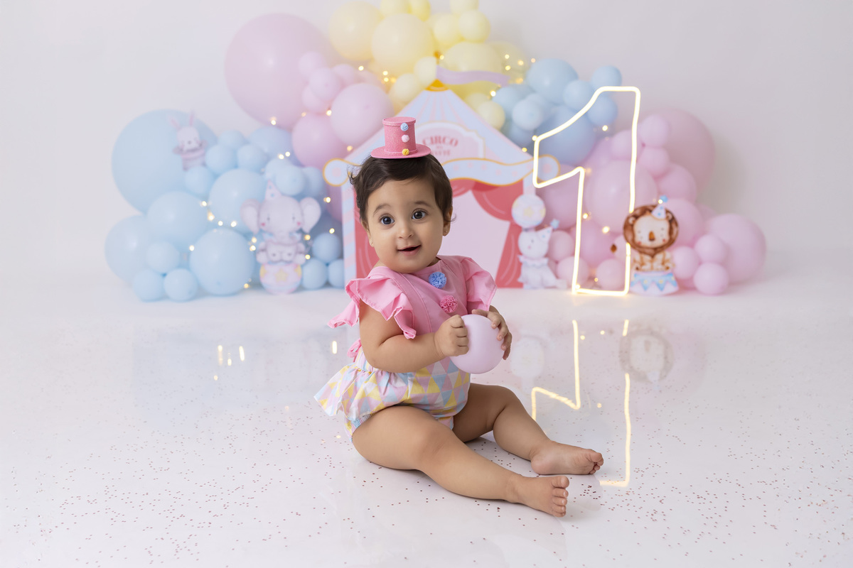 Bebê em ensaio Smash the Cake tema circo em estúdio fotográfico em Caraguatatuba, cenário colorido personalizado, bolo decorado, criança sorrindo e se divertindo durante sessão infantil