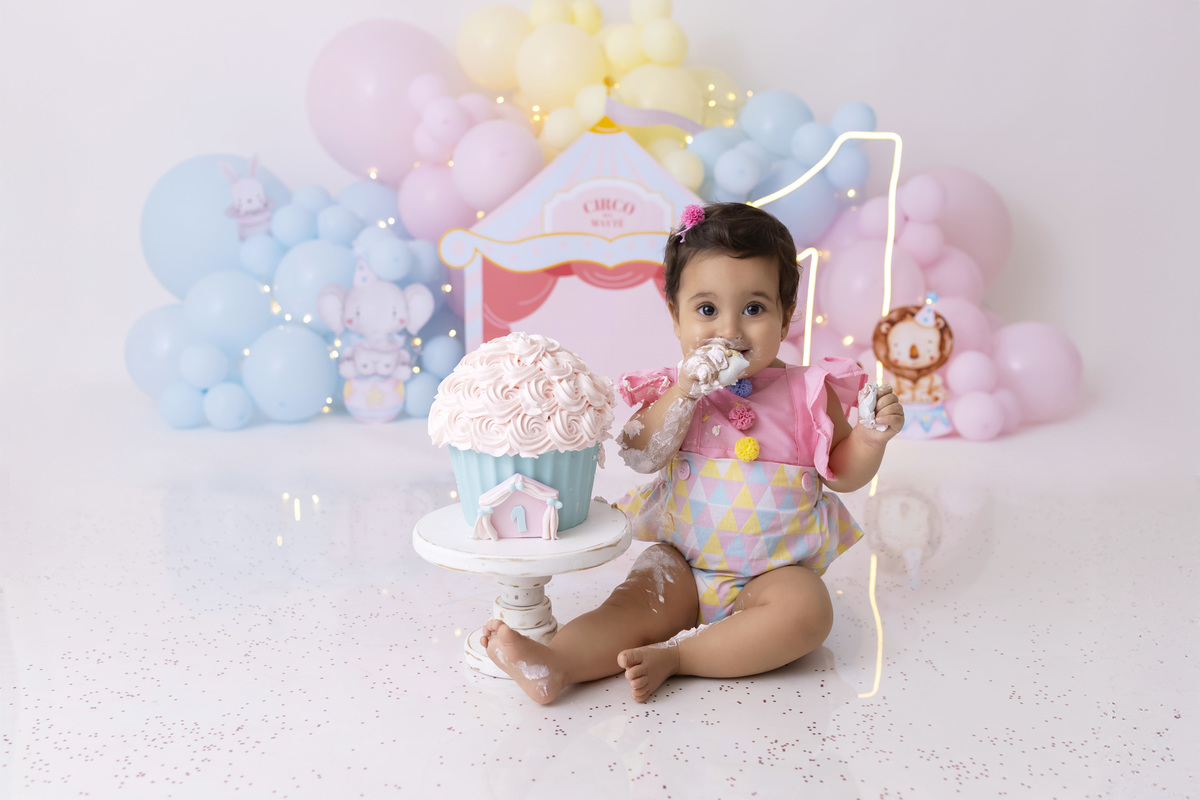 Bebê em ensaio Smash the Cake tema circo em estúdio fotográfico em Caraguatatuba, cenário colorido personalizado, bolo decorado, criança sorrindo e se divertindo durante sessão infantil